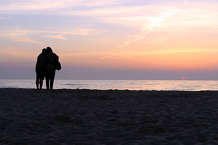 Paar guckt sich am Strand den Sonnenuntergang an