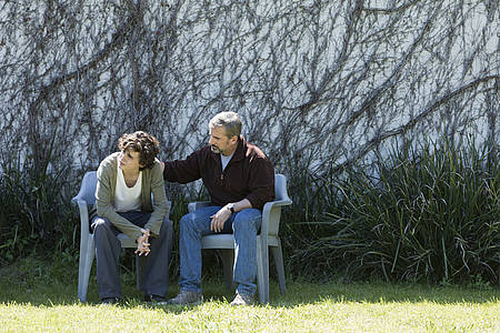 Hauptprotagonisten Nic und David sitzen auf einer Bank vor einer überwucherten Wand.